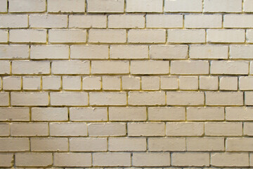 Frontal view of a wall of yellow old bricks of different sizes with harsh shadows. The bricks are mortar-bonded and cracked. Texture; background.