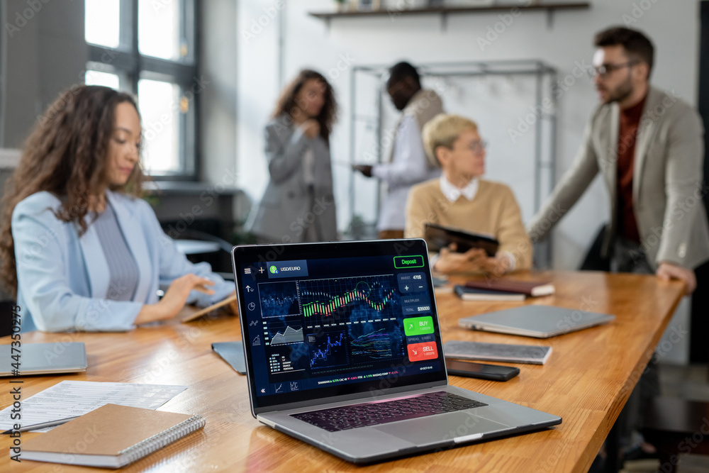 Aufkleber Laptop display with financial graph and other data on workplace where group of managers co-working