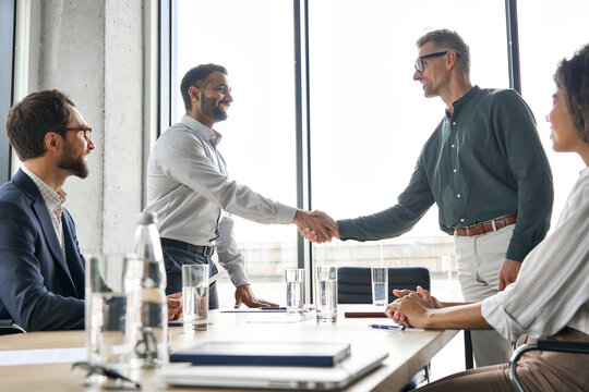 Two Happy Diverse Professional Business Men Executive Leaders Shaking Hands After Successful Financial Deal At Group Board Office Meeting. Trust Agreement Company Trade Partnership Handshake Concept.