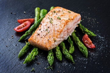 Traditional fried salmon filet with green asparagus and tomatoes served as close-up on a black board