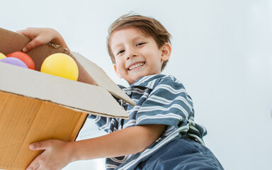 Naklejka premium Little Caucasian adorable cute boy playing colorful balls with fun and happiness, pouring them on camera with playful smile in living room at home on weekend holiday. Kid and Education Concept.