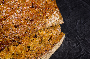 Slice of rustic natural yeast-free bread with flax, poppy seeds, sesame seeds, millet, pumpkin and sunflower seeds, on a black background, hard light, photo in a low key, close up.