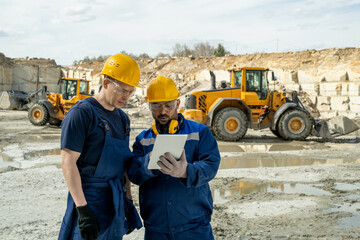 Two builders in workwear looking at sketch of building on tablet screen