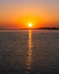 Hazy sun rising above the horizon, reflecting in a body of water. Long Island, New York