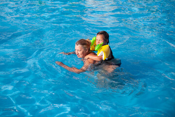 Grandmother and granddaughter in the pool. A girl in inflatable sleeves rides on the back of a young grandmother on a sea family vacation. 