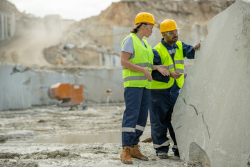 Two builders in hardhats and workwear discussing working points by huge block