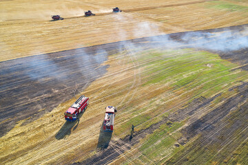 Rescuers extinguish the fire during the summer harvest in the field