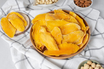 Wooden bowl dried mango fruit slices. Nuts: cashews, almonds, hazelnuts on light background....