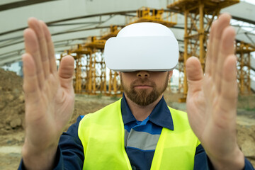 Young construction worker gesturing on construction site he using virtual reality glasses