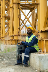 Portrait of African construction worker in workwear looking at camera while sitting outdoors with...