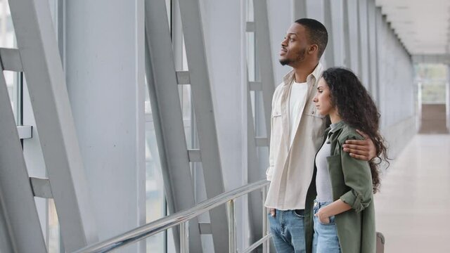 Multiracial couple newlyweds afro american man african husband and hispanic woman curly wife stand embracing at airport terminal talk looking window before boarding plane honeymoon travel trip abroad