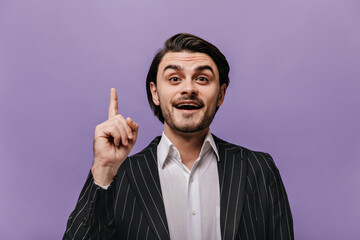 Gorgeous young brunette in business suit having idea and showing forefinger while looking into camera. Man posing against violet background