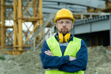 Portrait of builder in protective workwear standing with arms crossed outdoors and looking at camera