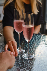A glasses of rose wine in the hands of a girl and man who relaxing on restaurant terrace. Summer holiday. Celebrate and enjoy moment. Alcoholic drink tasting. Romantic evening aperitif