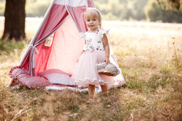 cute little girl is having fun near wigwam in a summer field on sunny day. Young family spending time together on vacation, outdoors. The concept of summer holiday © Andriy Medvediuk
