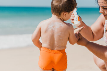 Mother putting sunscreen cream to toddler son