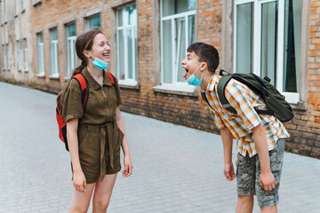 Schoolboy and schoolgirl posing on the way to school. They play, laugh and fool around. Wearing a protective mask on their faces from a coronavirus infection. Education and back to school concept.