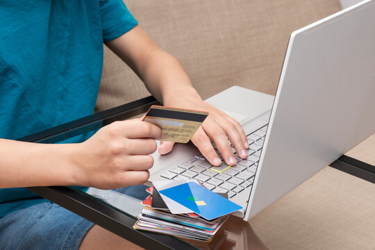 Close up image of child's hands holding credit card in front of laptop making online payment. New reality, online shopping.