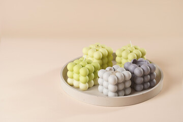 A pastel yellow, green and grey bubble candles on a concrete tray on a beige colored background