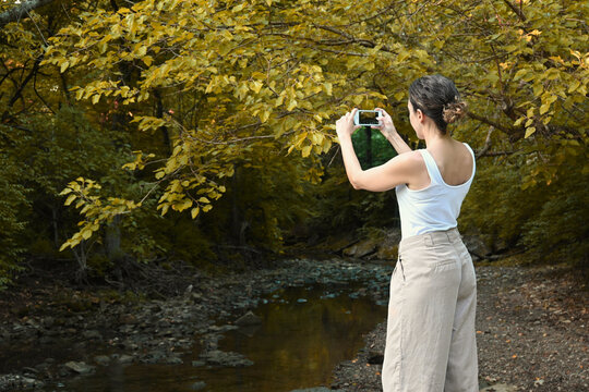 Young latin woman taking a picture with smartphone of an autumn landscape