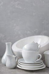 Empty crockery set or ceramic dishes. White kitchen dishware and tableware on table near grey wall