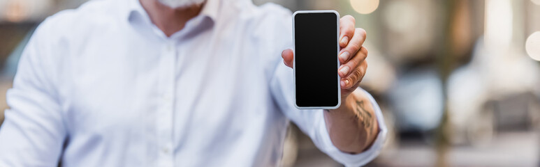 cropped view of middle aged man holding cellphone with blank screen, banner