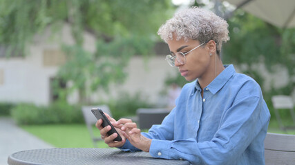 Obraz premium African Woman using Smartphone in Outdoor Cafe
