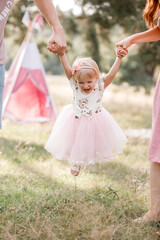 View on toddler. Mother, father hold hands daughter enjoy nature and walk in the park. Young family spending time together on vacation, outdoors. The concept of family summer holiday.