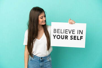 Young caucasian woman isolated on blue background holding a placard with text Believe In Your Self