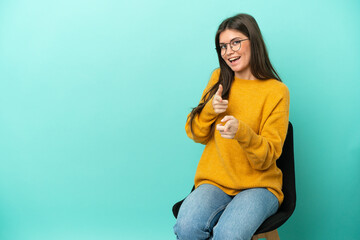 Young caucasian woman sitting on a chair isolated on blue background pointing to the front and smiling - Powered by Adobe