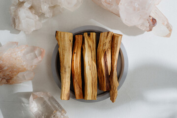 Palo Santo sticks on a concrete plate and natural crystals, beautifully illuminated by sunlight. Set of incense for fumigation. Top view. Organic sacred tree incense from Latin America. - obrazy, fototapety, plakaty