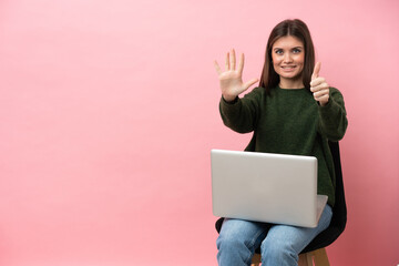 Young caucasian woman sitting on a chair with her laptop isolated on pink background counting six with fingers