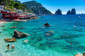 CAPRI, ITALY - JUNE 15, 2021: Tourists visit Marina Piccola Beach with a view on famous Faraglioni.