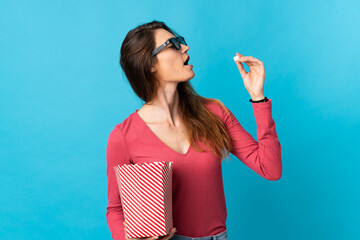 Young Ireland woman isolated on blue background with 3d glasses and holding a big bucket of popcorns