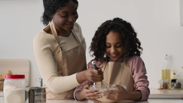 African american mother and daughter cooking dough together at kitchen, woman taking daugh and messing girl's nose