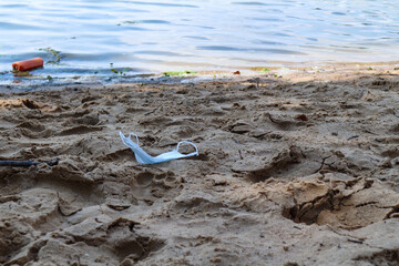 Fototapeta na wymiar the medical mask is lying on the beach, on the sand