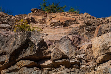 Granite rocks close-up on background blue sky with white clouds, green leaves on treetops.