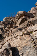 Granite rocks close-up on background blue sky with white clouds, green leaves on treetops.
