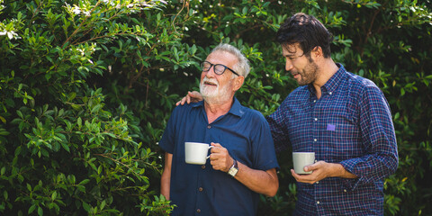 adult son and elderly senior father talking together and holding coffee cup in the garden, happy...
