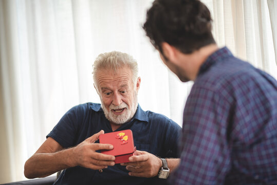 caucasian man surprise him adult father with giving gift box to celebration at home, family present to happy together lifestyle with love, people having fun and smiling in holiday