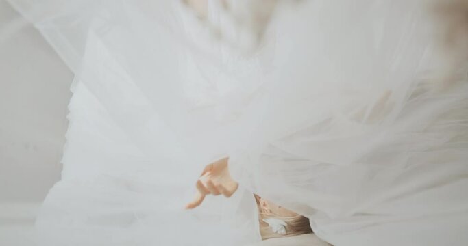 A serene scene of a bride in a white wedding dress lying down with her eyes closed, surrounded by soft tulle fabric. The ethereal setting exudes calmness and elegance,