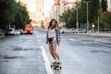 Pretty woman riding on a skateboard on an empty city road early in morning