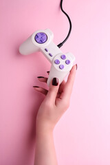Woman holding video game joystick on pink background, closeup. Game addicted concept. Cropped photo...