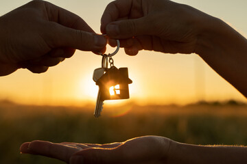Close-up female gives a man the key to a new house on the background of a beautiful sunset. The...