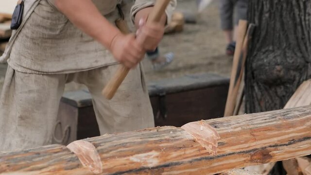 Man lumberjack cutting large log with axe - wood shavings, chips flying at summer historical medival festival - close up, slow motion. Craftsmanship, revival, reenactment, handwork concept