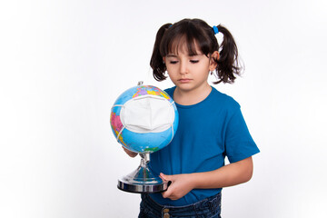 mistrustful and sad preschool girl child holds terrestrial globe with fabric mask protection covid,...