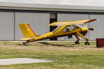 Yellow vintage plane on the airfield view from the side near hangar. Aircraft for active extreme sport. Conventionally laid out single-engine, high-wing light aircraft with seating for two