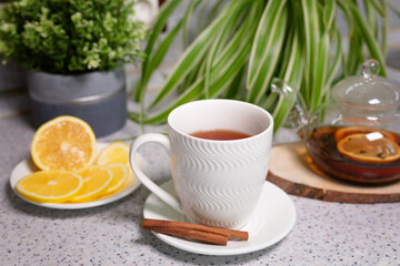 Fototapeta na wymiar A hot tea drink with lemon and orange, a teapot and a white cup, served with delicious lemon and cinnamon. Fragrant and warming tea