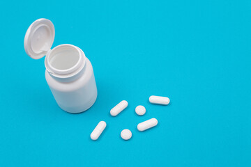 Fototapeta na wymiar Global Pharmaceutical Industry and Medicinal Products - White Pills or Tablets Scattered from the Pill Container, Lying on Blue Background