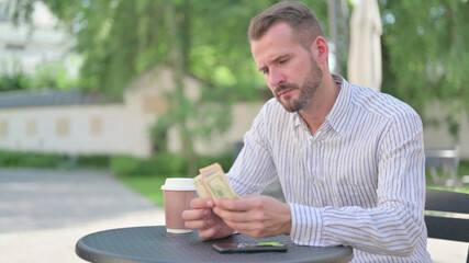 Fototapeta premium Mature Adult Man Counting Dollars while Sitting in Outdoor Cafe